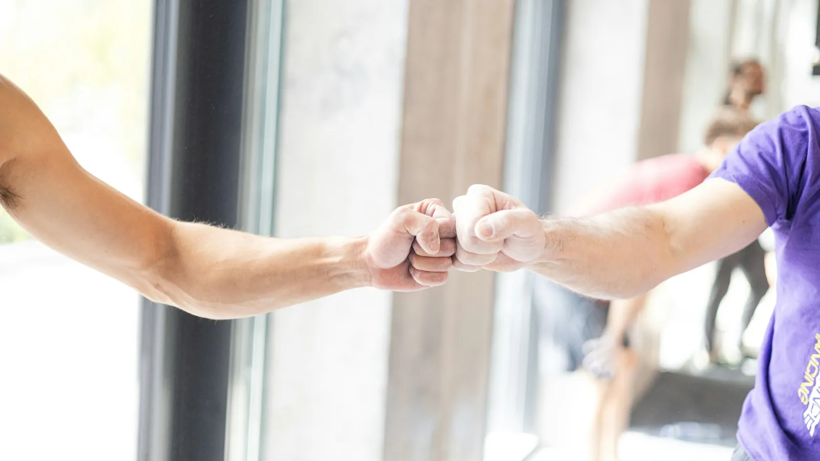 Two people fist bumping in a gym, the belonging signal that makes a fitness community visible
