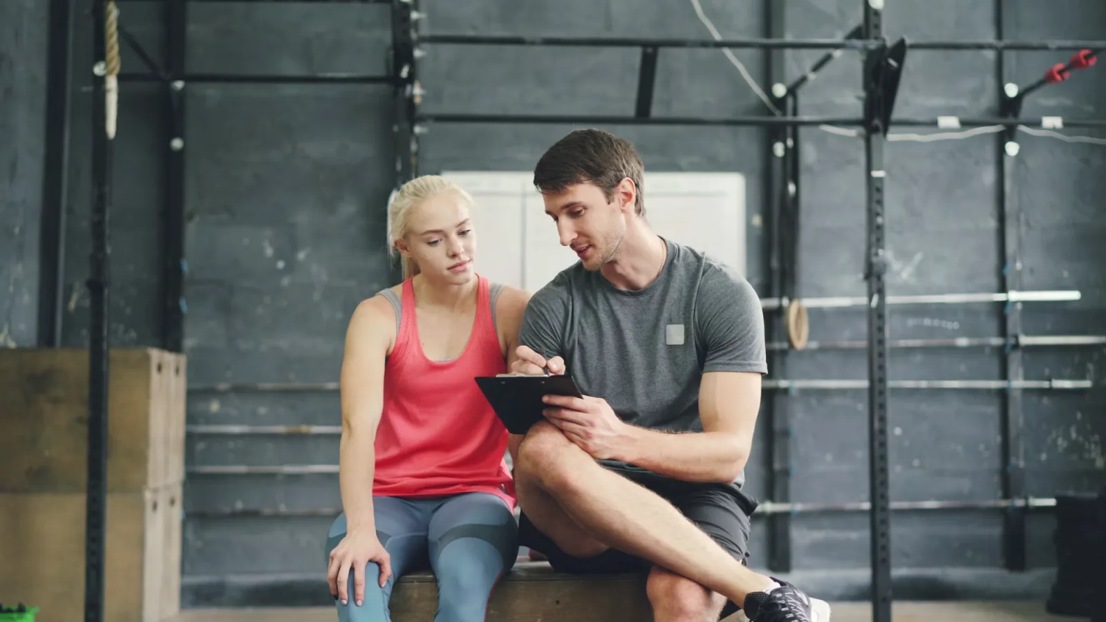 Personal trainer reviewing a coaching plan with a client on a clipboard in a gym