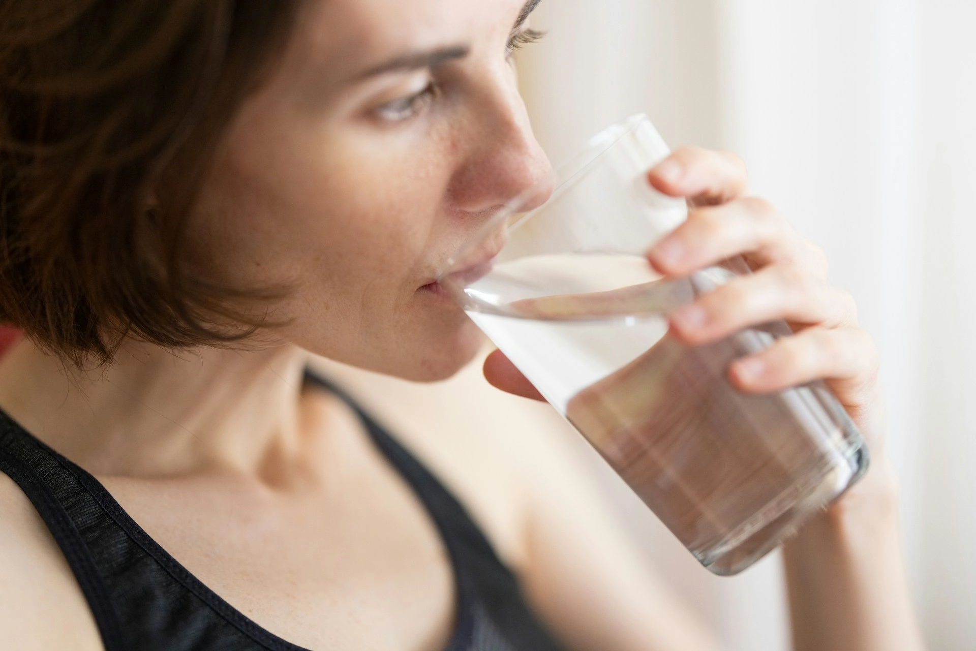 Client in workout gear drinking a glass of water at home, the kind of daily habit online coaches assign between sessions