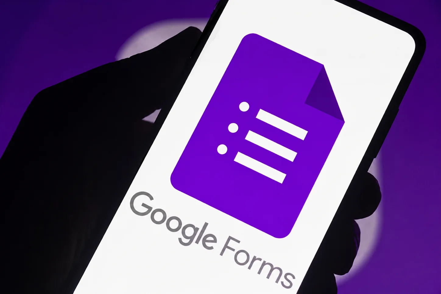 Hand holding a phone showing the Google Forms logo, the free tool most coaches start their client check-ins with