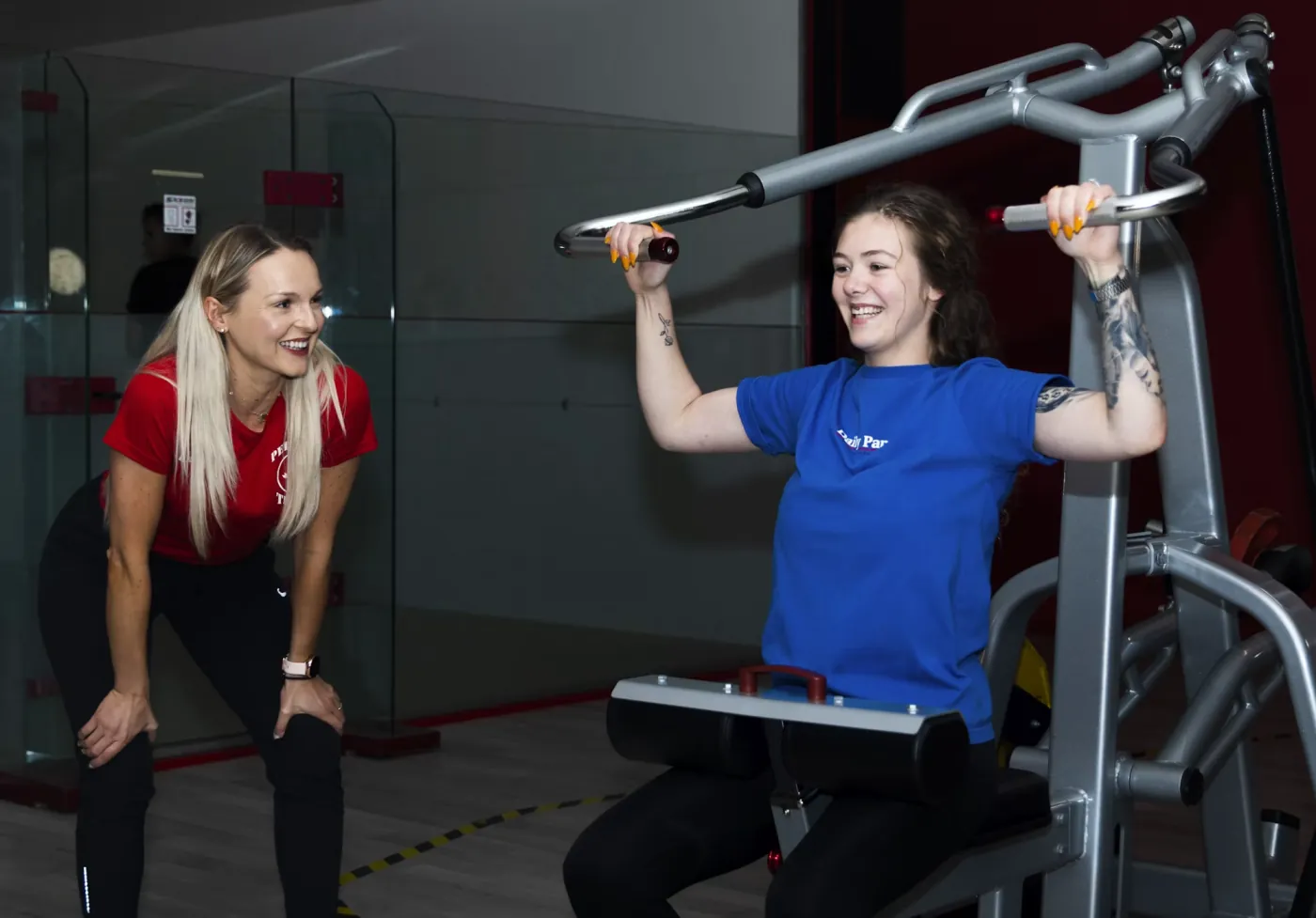 Personal trainer smiling and encouraging a client through a set on a lat pulldown machine, part of the training block the coach built for her