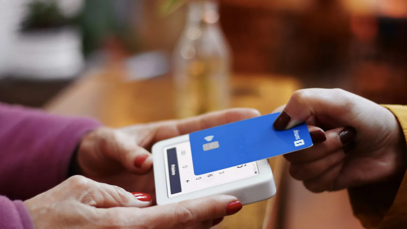 One person handing a blue bank card to another over a handheld card terminal, the moment a coaching package is paid