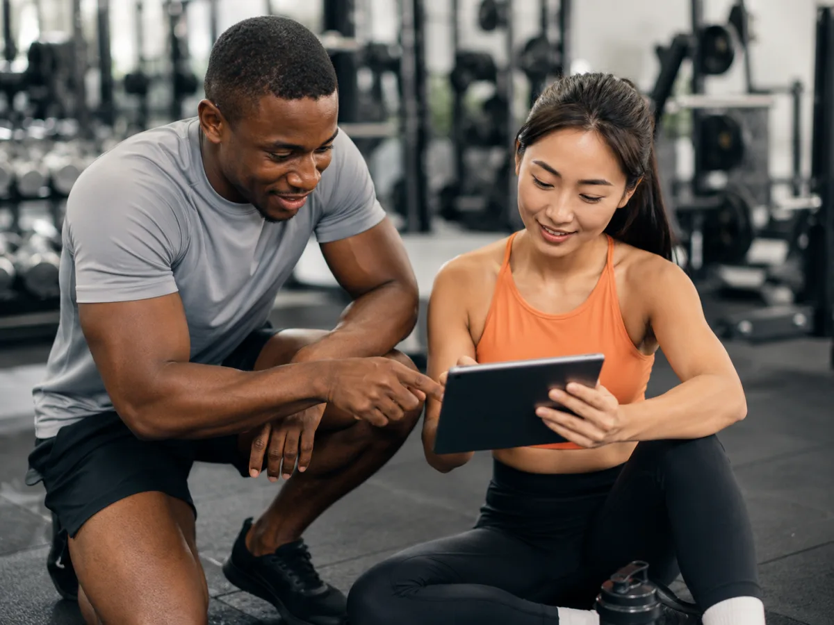 Personal trainer and client reviewing a coaching plan on a tablet together in a gym