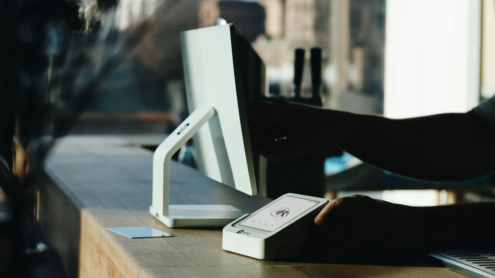 A card payment terminal beside a point-of-sale screen on a cafe counter, the point where a separate card surcharge used to be added