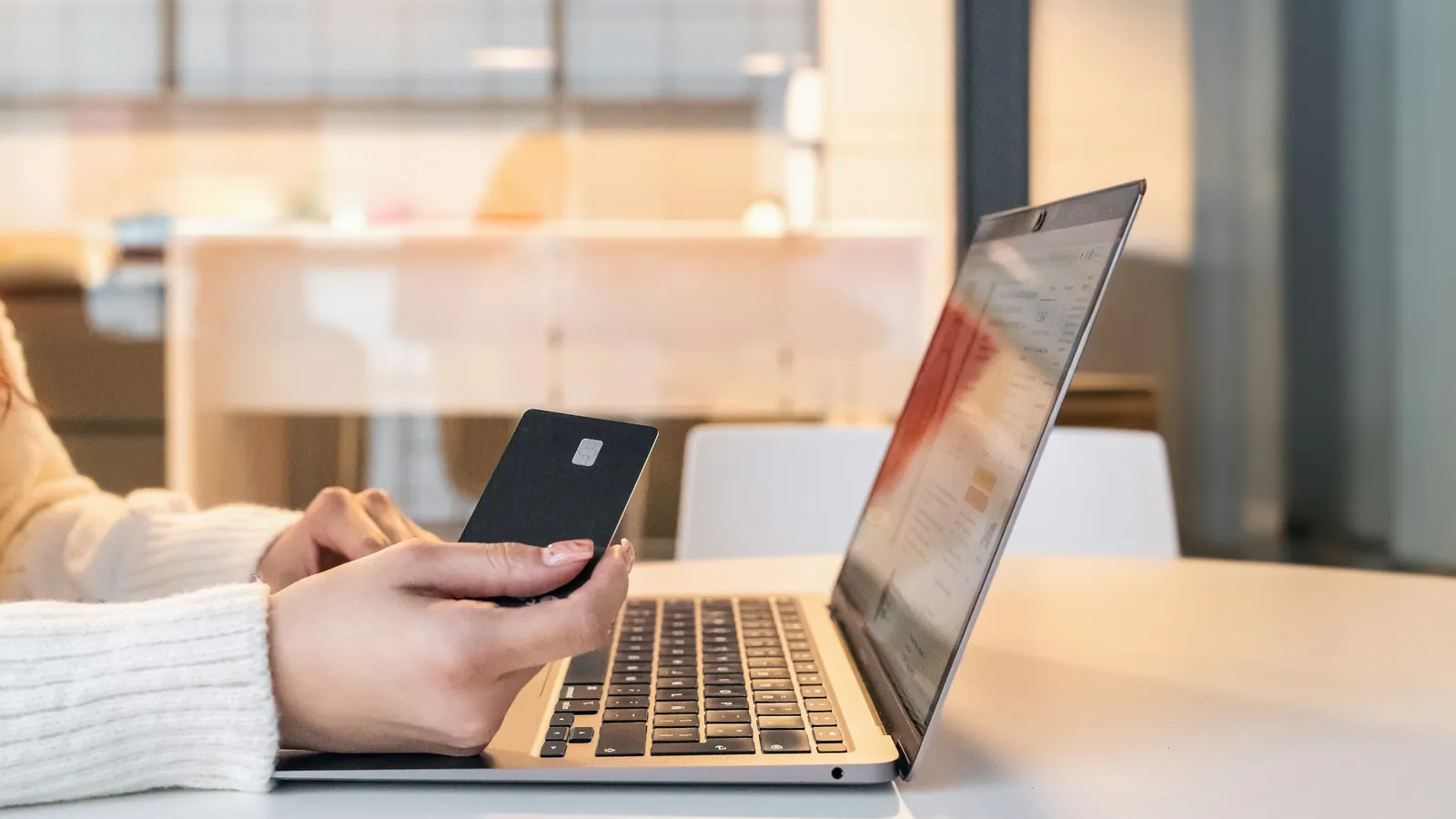A person holding a bank card beside an open laptop, about to pay online