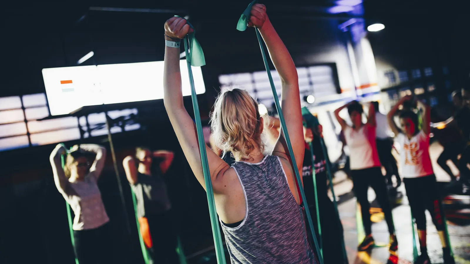 A group fitness class working through a resistance-band drill together in a gym, the kind of squad a coach programmes for as one Client Group