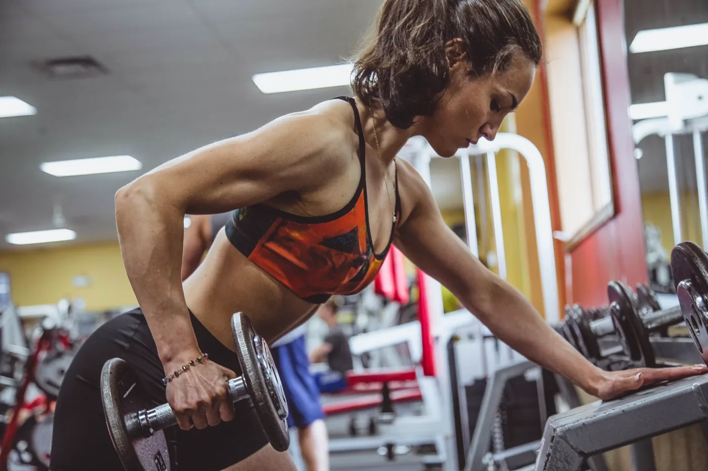 Woman performing a single-arm dumbbell row in the gym, working through a programmed set and rep range from her online coach