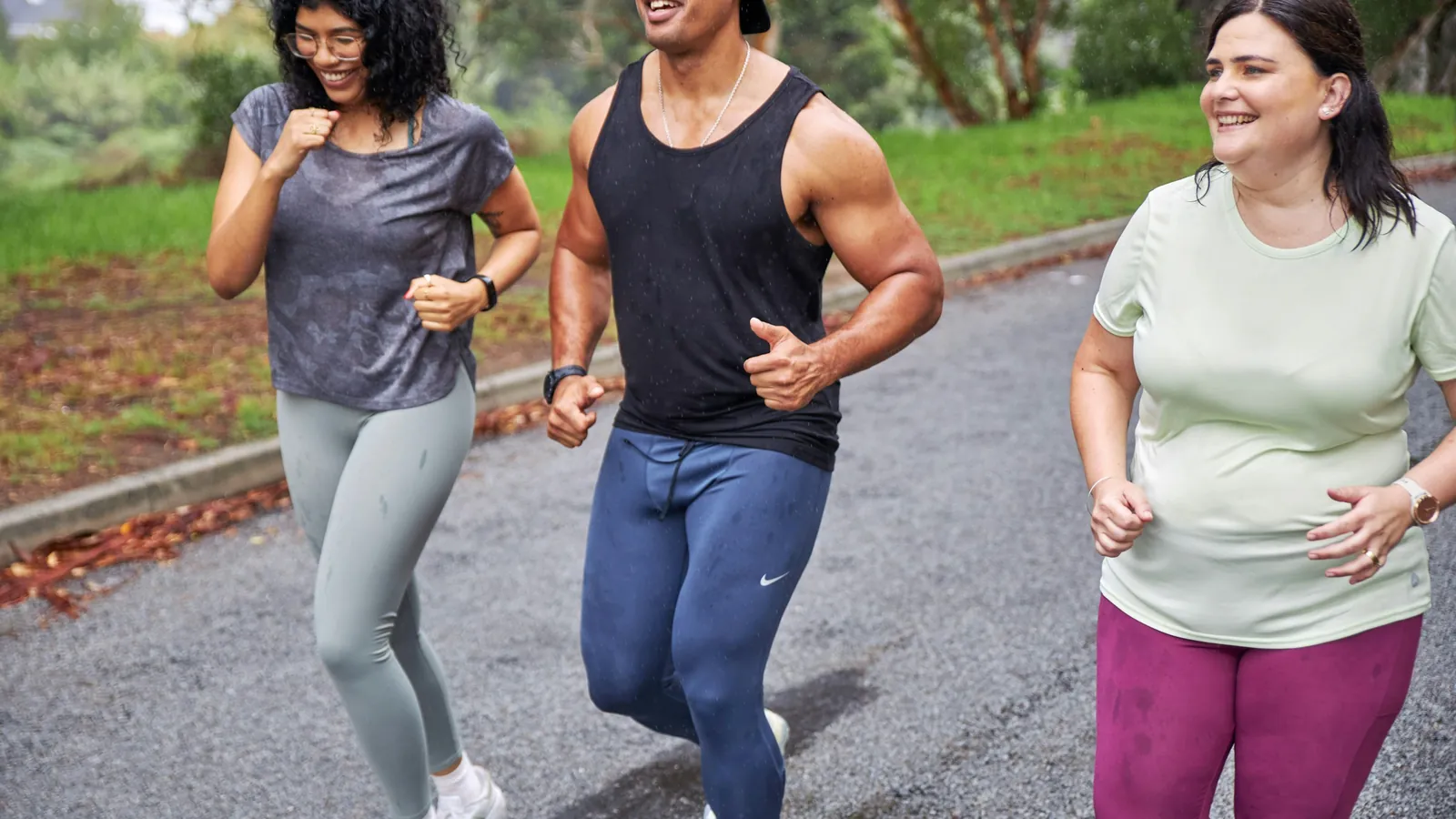 Three people running together along a wet outdoor path, the kind of coached cohort an online fitness challenge brings together