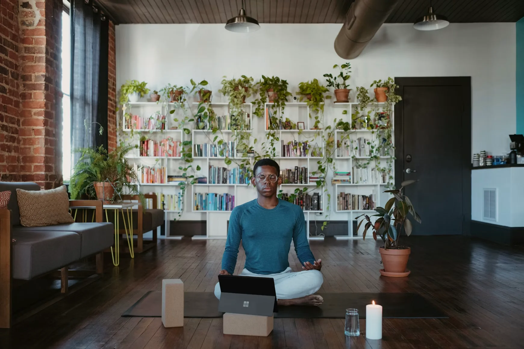 Coach sitting cross-legged on a yoga mat with a laptop open in a home studio