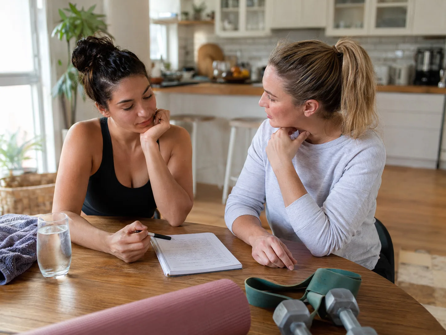 Online coach and client reviewing a training notebook and check-in at a kitchen table